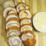 Sliced cordon bleu sitting on top of wooden board with white sauce dip on the side.