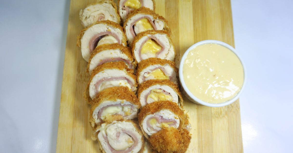 Sliced cordon bleu sitting on top of wooden board with white sauce dip on the side.