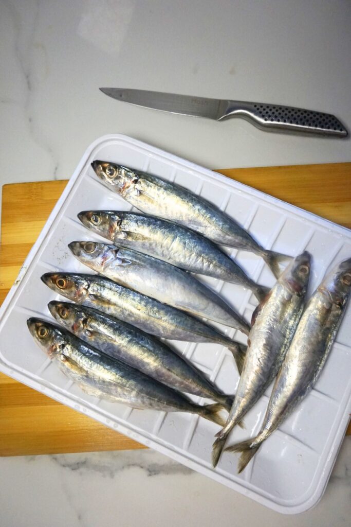 Fresh galunggong in a white plastic plate on top of a wooden board, knife on the side.