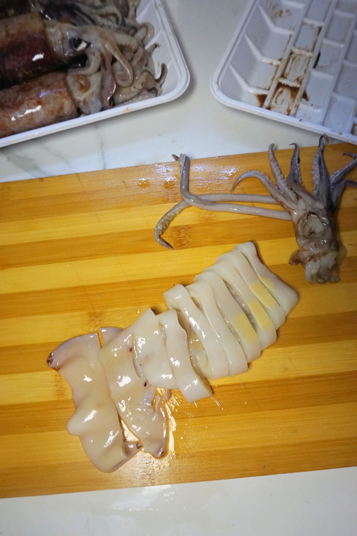 Clean squid tube being sliced into even rings on a chopping board.