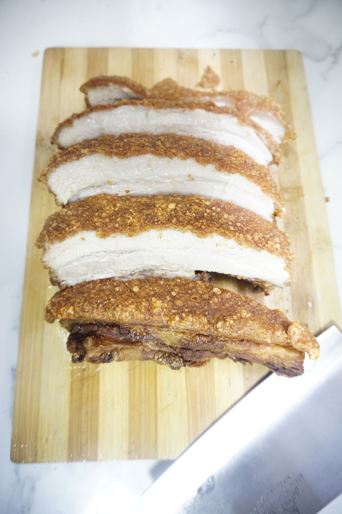 Freshly fried crispy lechon belly sliced sitting on top of wooden board.