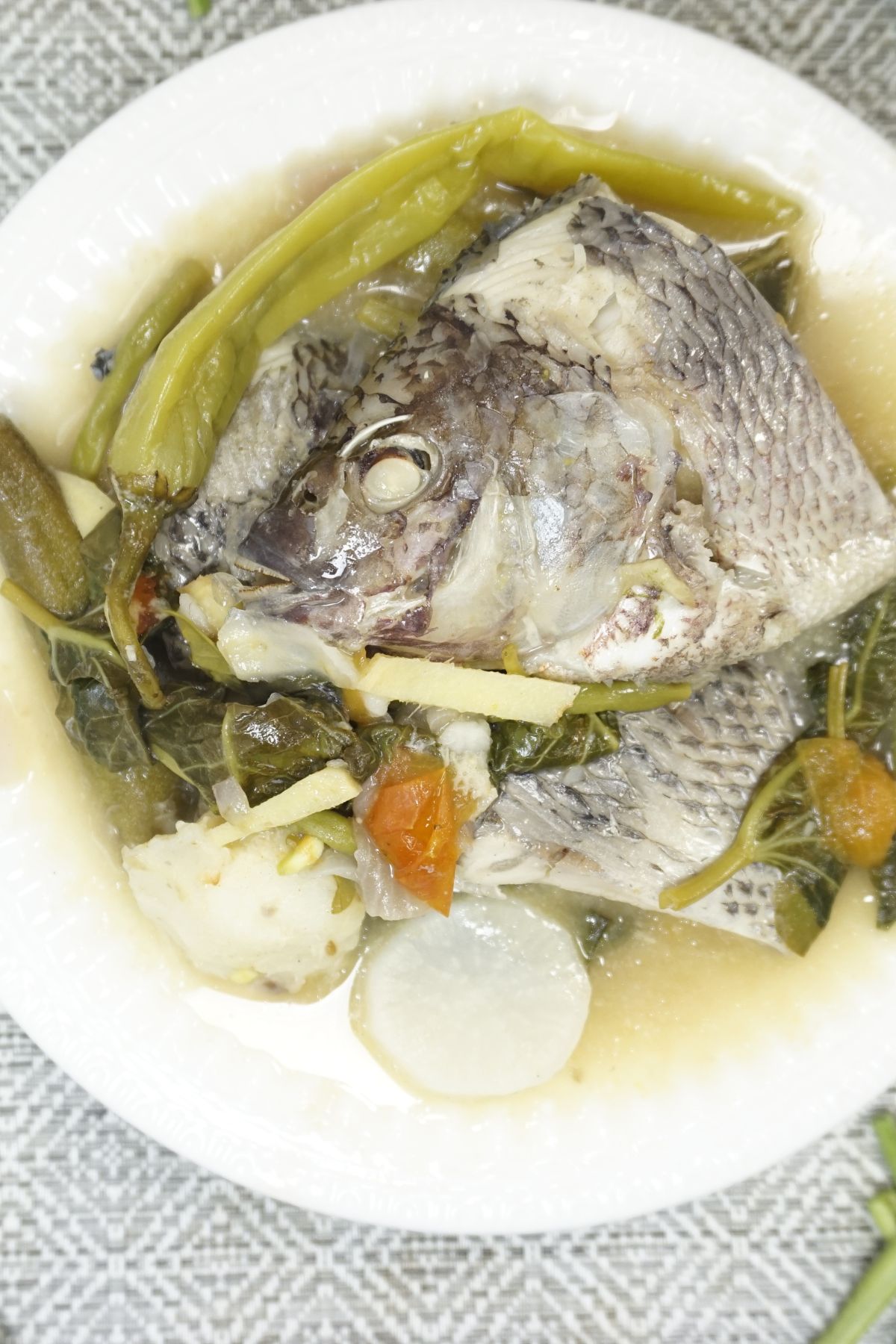 Overhead shot of a serving of sinigang na tilapia in a white bowl.