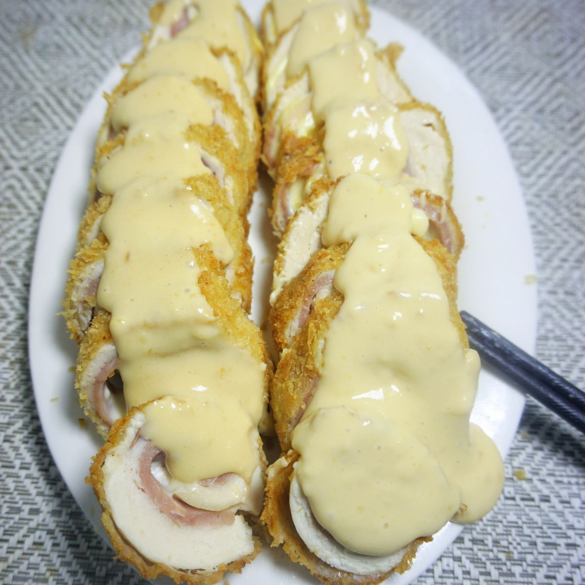 Cheese sauce covered sliced cordon bleu in a white plate.