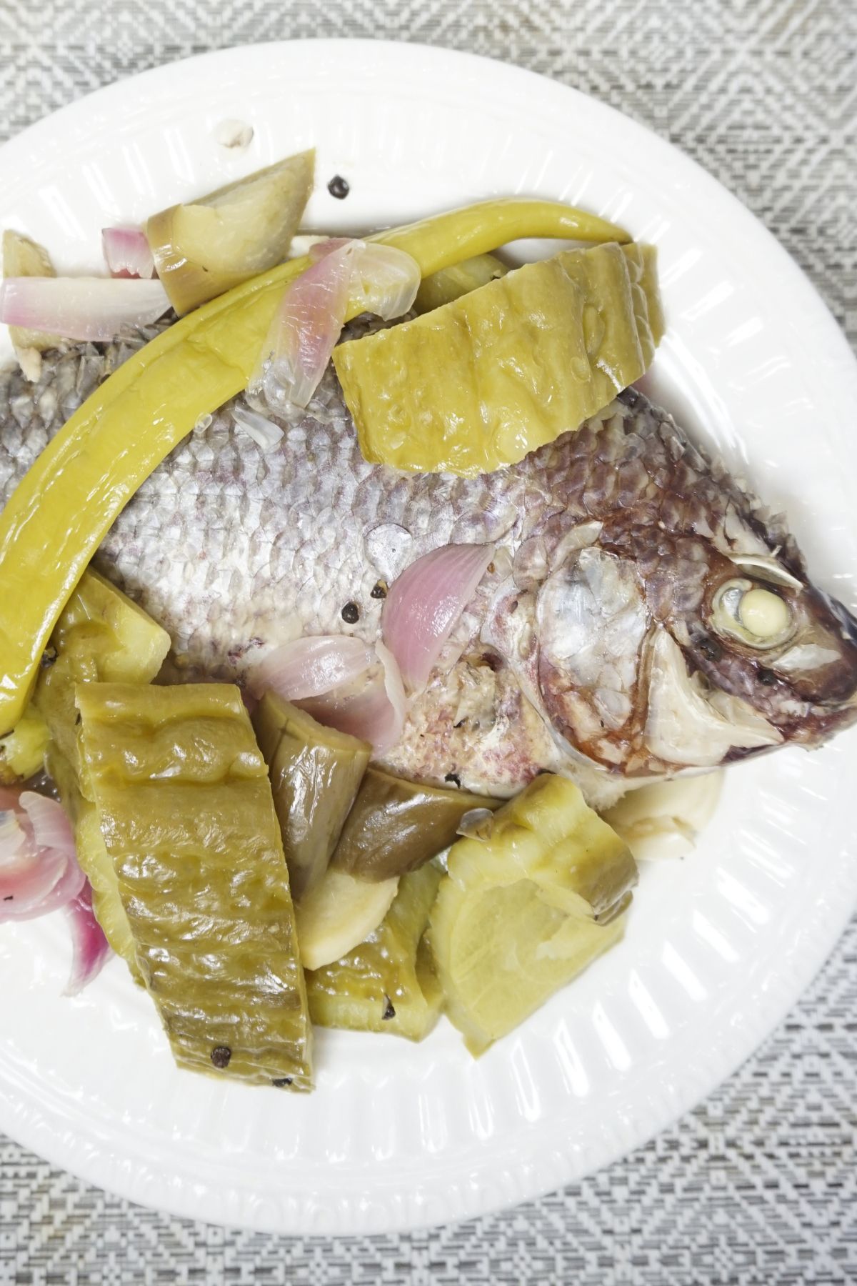 Paksiw na tliapia served in a white plate with eggplant and bittermelon slices.