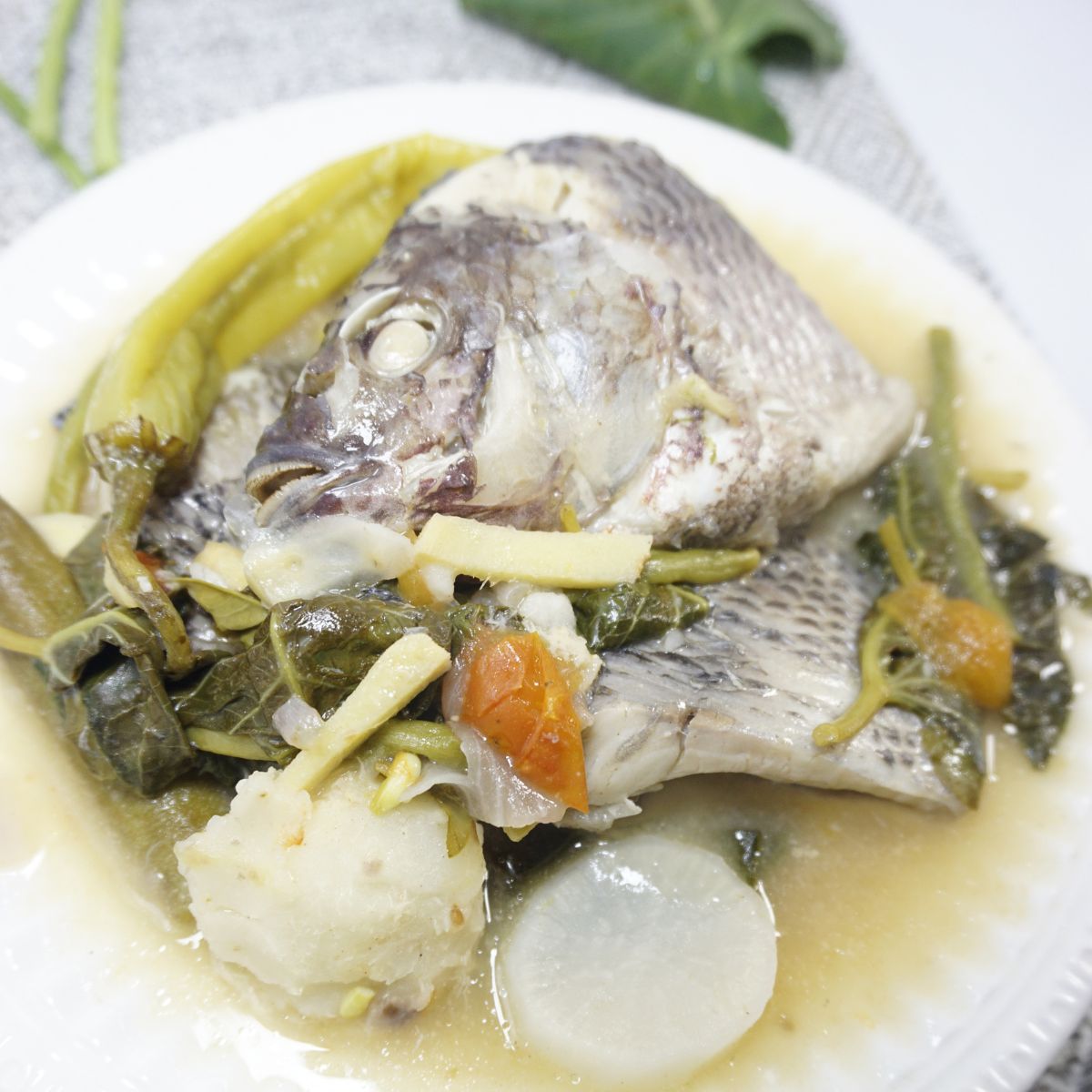 Sinigang na tilapia with vegetables served in a white bowl.