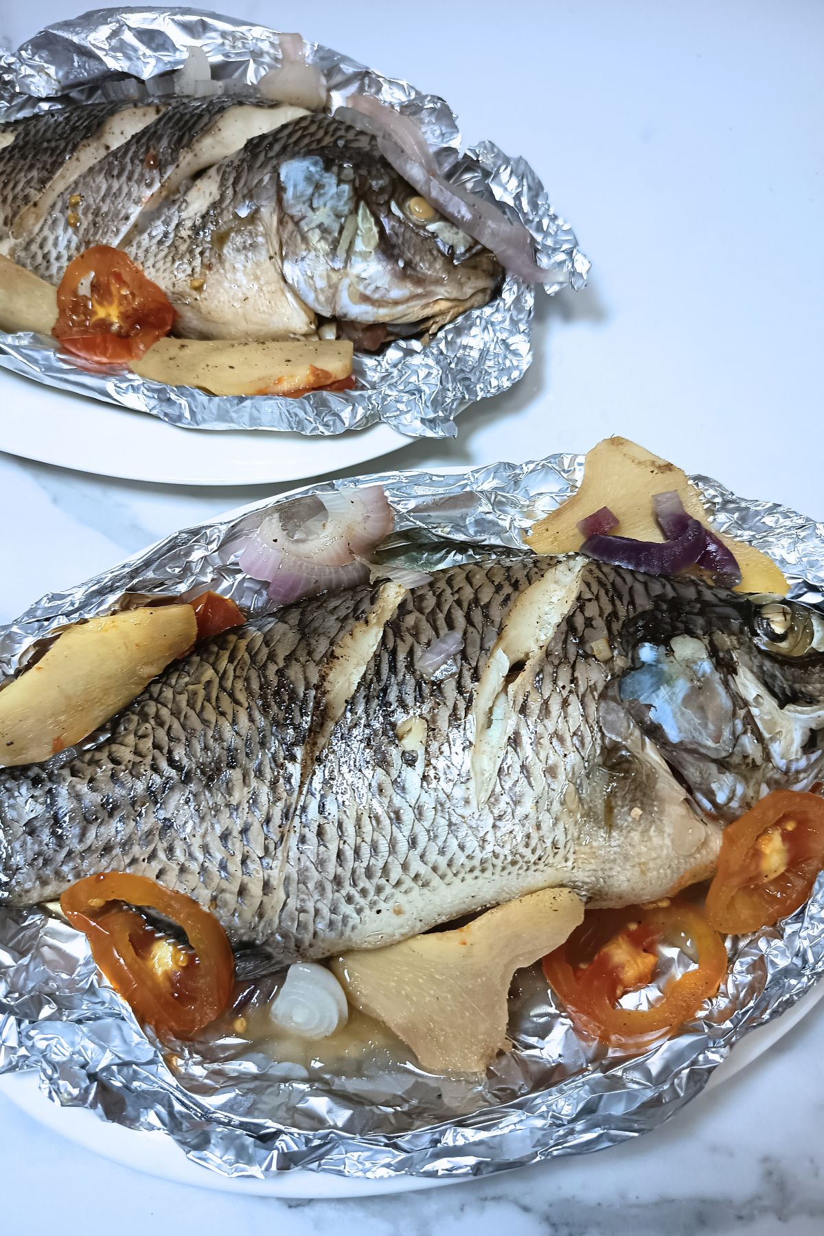Steamed tilapia in a foil topped with sliced ginger and tomatoes