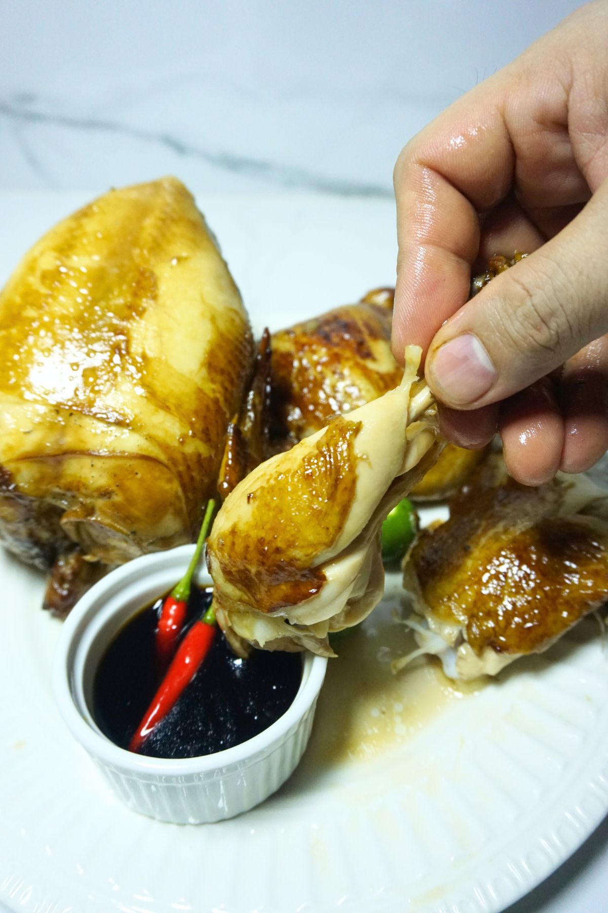 Hand holding chicken drumstick dipped to toyo mansi