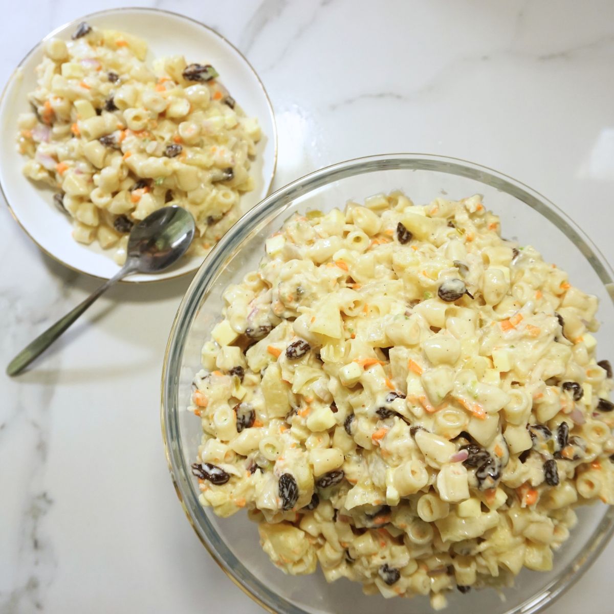 Macaroni salad in a glass bowl and a serving in a saucer