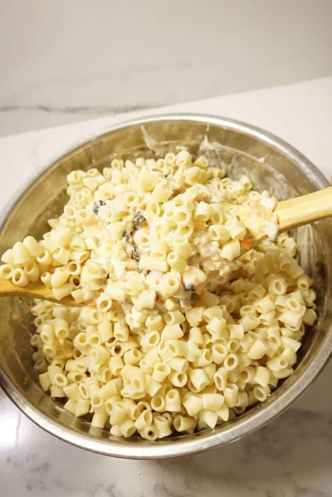 Mixing of macaroni salad and ingredients in a metal bowl.