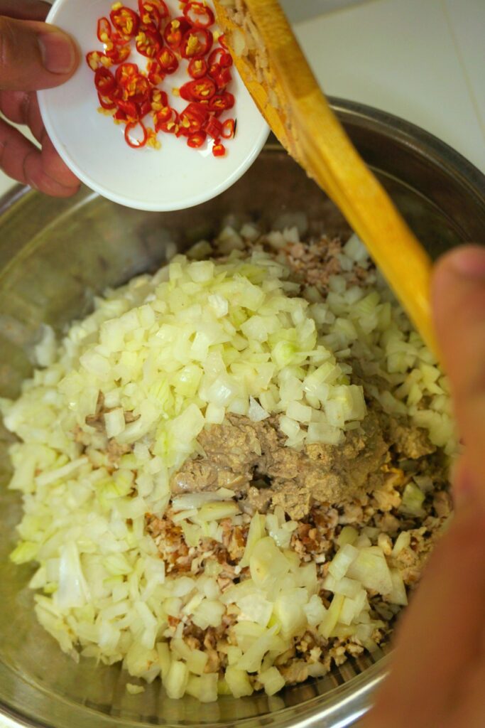 Chopped grilled pork belly combined with white onion and chopped chilis in a metal bowl.