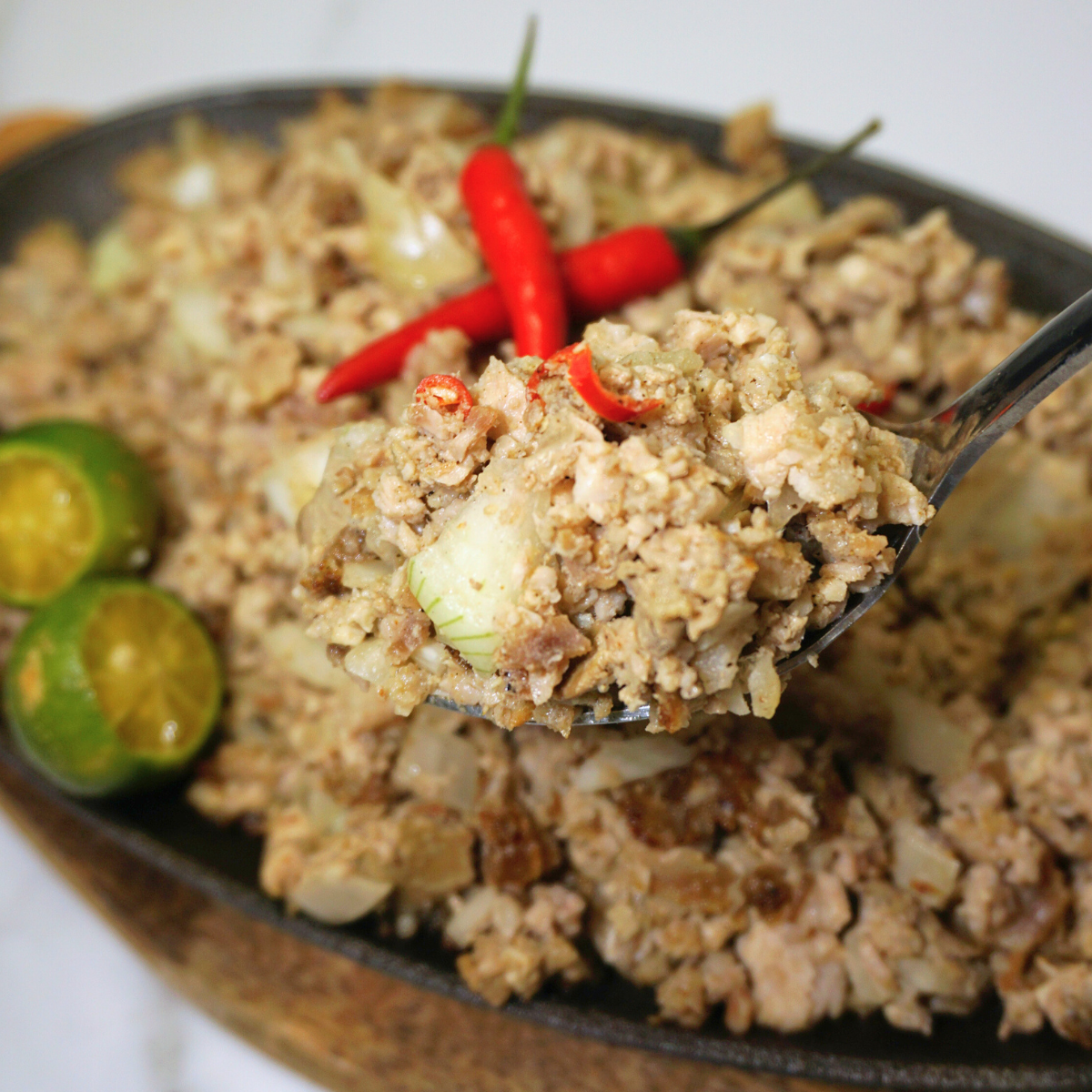 Sisig scooped with a spoon serving in a sizzling plate.